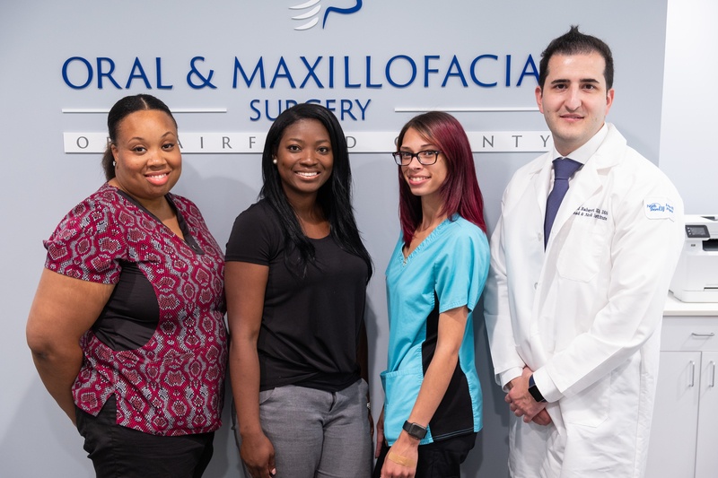 oral and maxillofacial surgery staff of four, smiling in front the office logo